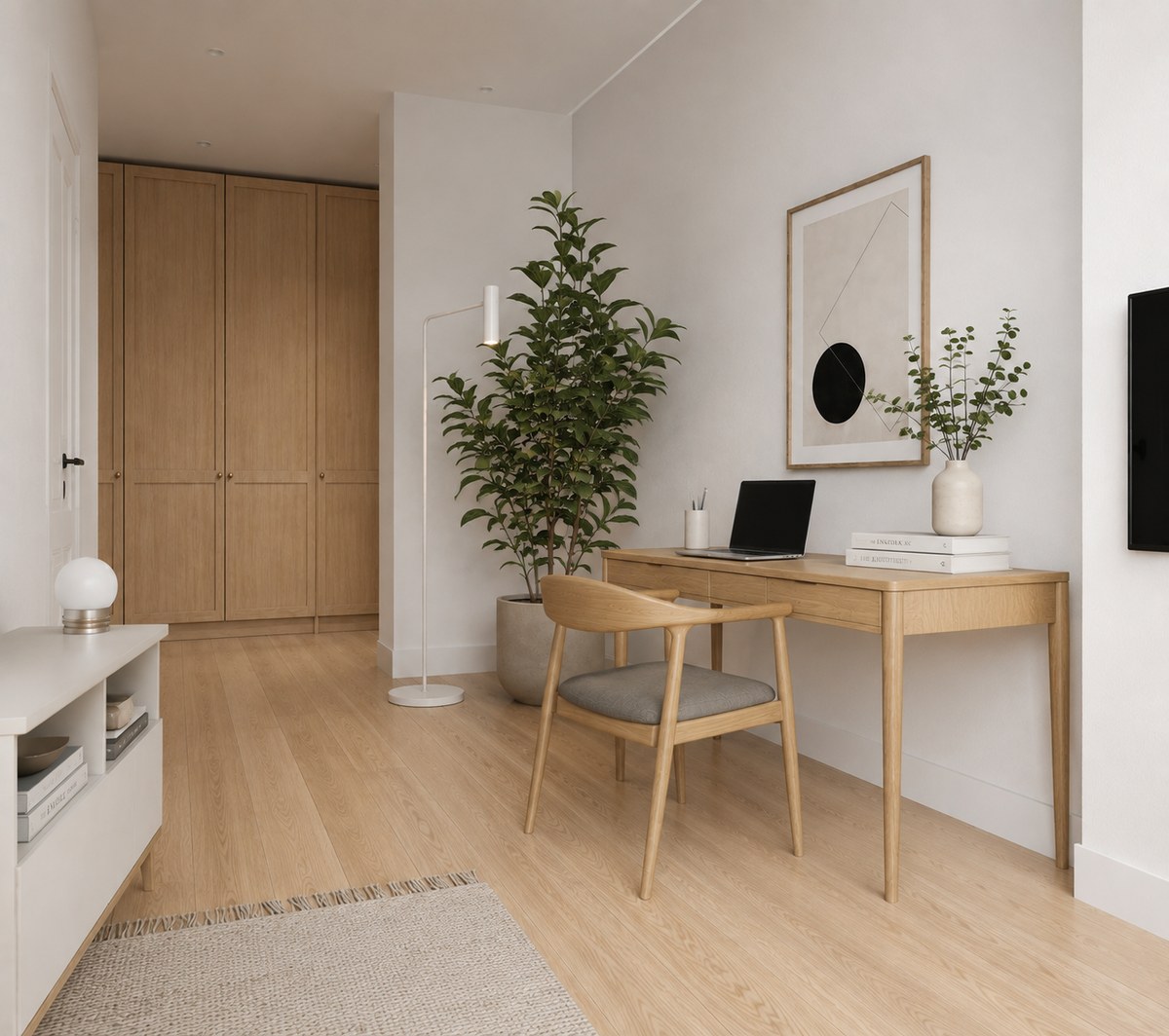 A room shot from a different corner: a pale oak wardrobe with three doors on the back wall, a white door and corridor at the far left, the desk and chair against the right wall under a framed print, a tall plant beside a floor lamp, recessed downlights in the ceiling